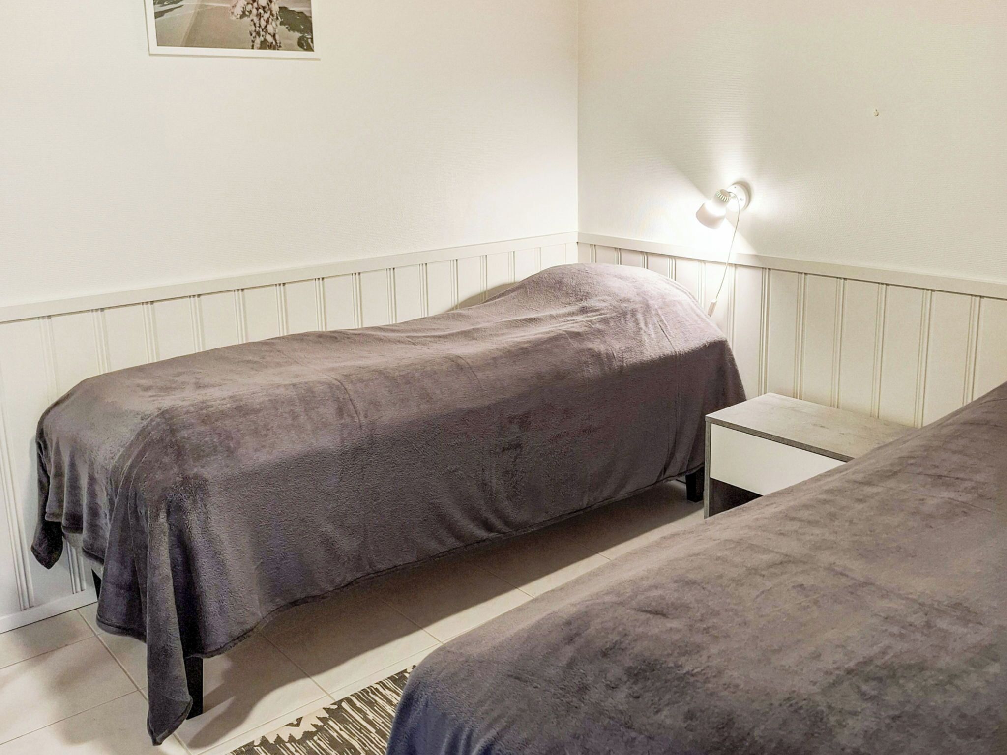 Una habitación sencilla con dos camas individuales, una mesita de noche, una lámpara y una alfombra.
