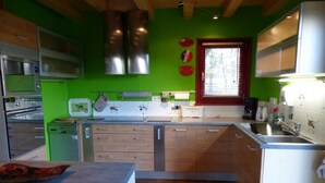 Een keuken met groene wanden, houten keukenkastjes, roestvrijstalen apparatuur en een raam met jaloezieën.