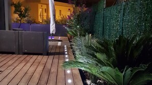 A wooden deck with a row of lights, surrounded by greenery and a building in the background. - COSY BEDROOM 23m2. Adults Only (agde)