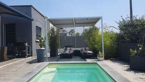 A swimming pool with a covered seating area and a modern building in the background. - COSY BEDROOM 23m2. Adults Only (agde)