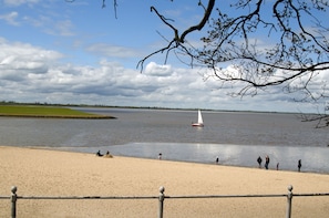 A sandy beach with a calm body of water, a sailboat, and people by the shore. - Vacation home Nemo, holiday apartment rental North Sea - Holiday home Nemo (Varel)