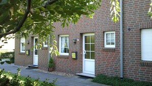 A brick building with multiple windows and doors, a small tree in the foreground, and a paved driveway. - Vacation home Nemo, holiday apartment rental North Sea - Holiday home Nemo (Varel)