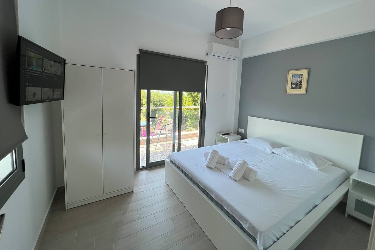 A modern bedroom with a bed, a television, a wardrobe, and a balcony with outdoor furniture.