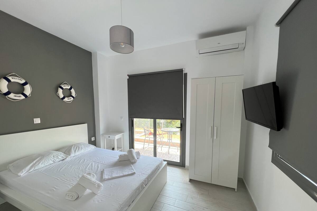 A modern hotel room with a neatly made bed, a small desk, a wardrobe, and a TV mounted on the wall.
