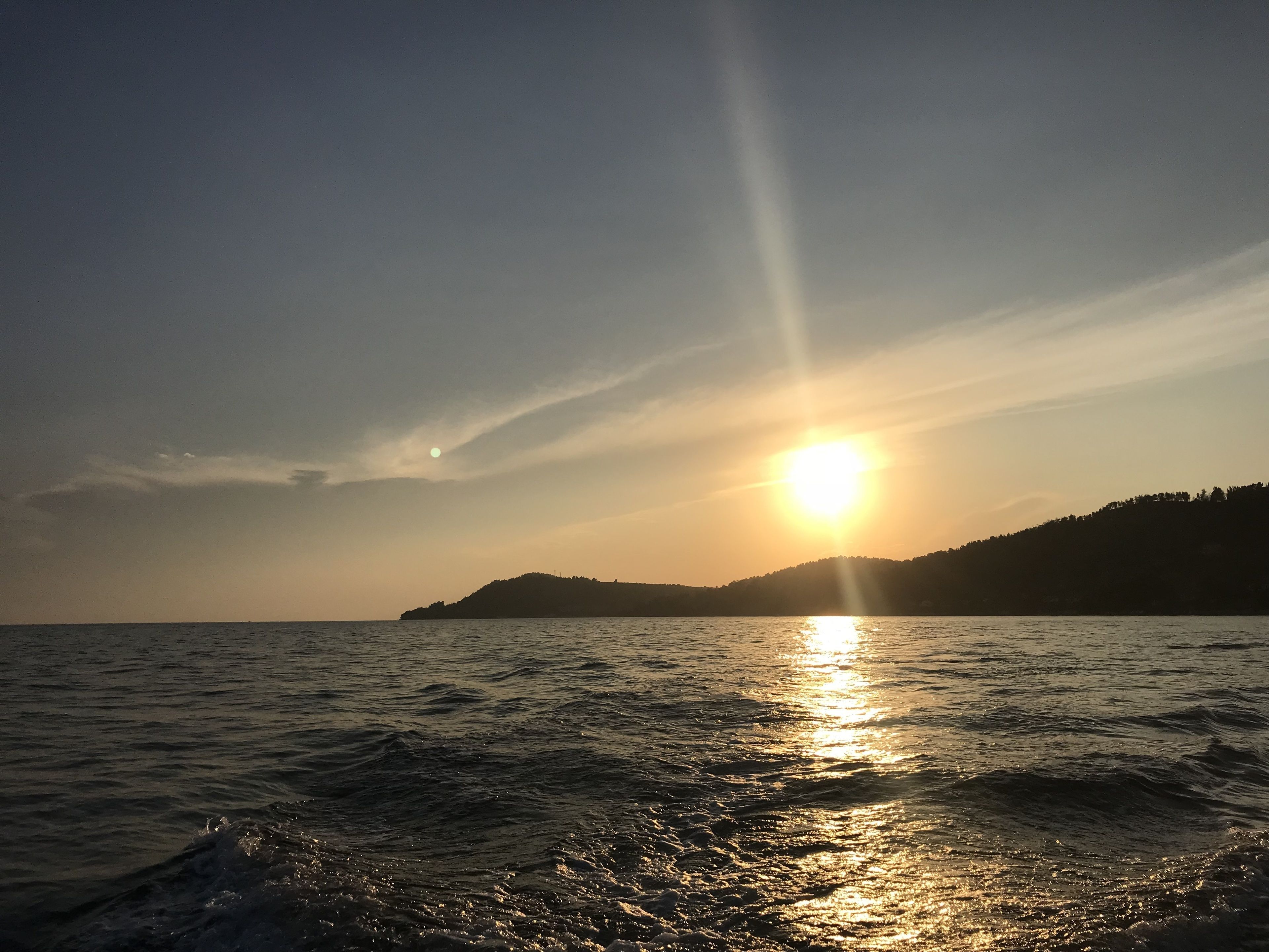 Un coucher de soleil sur une étendue d’eau, avec une masse terrestre visible au loin.