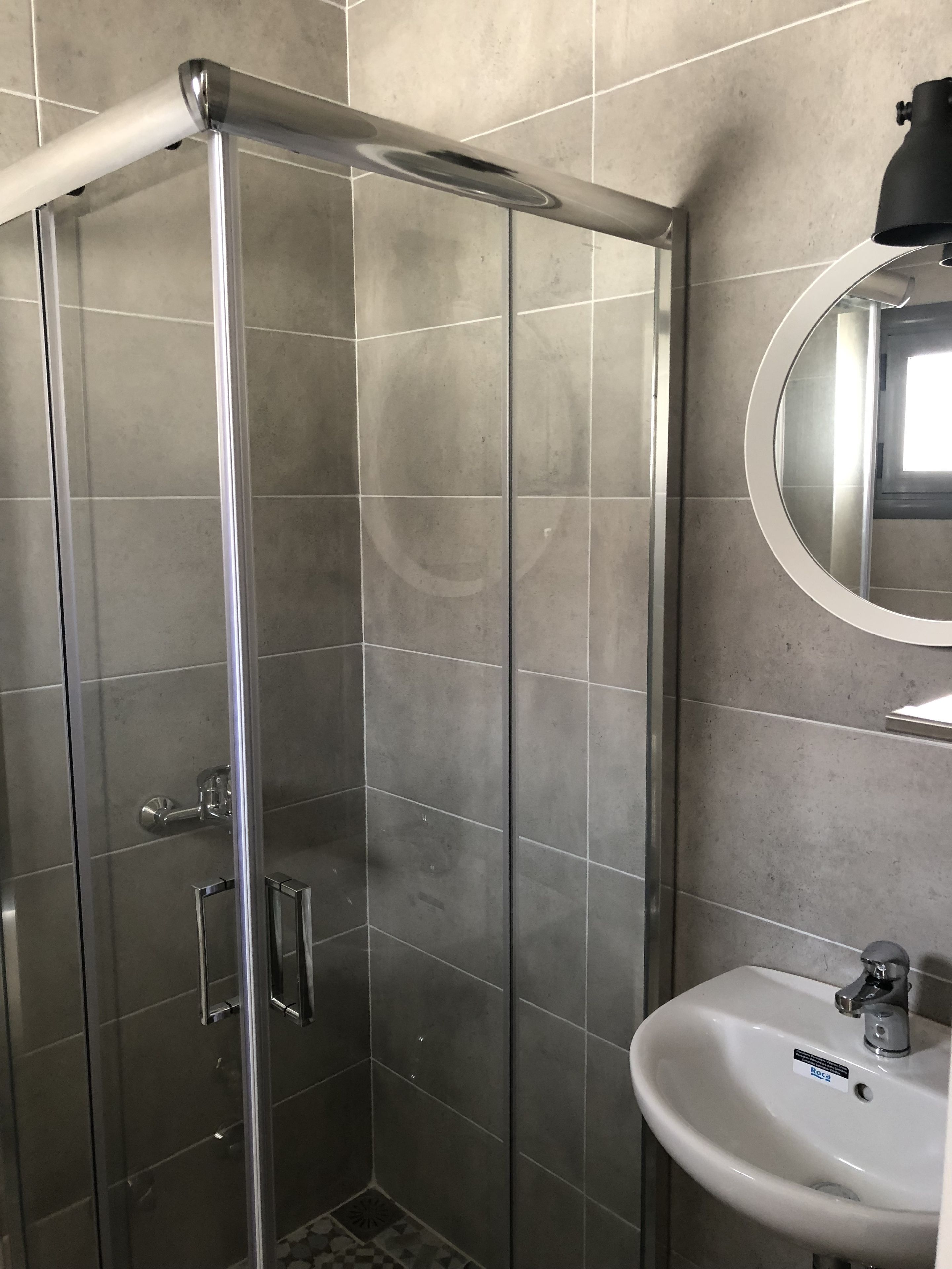 A bathroom with a glass-enclosed shower, a white sink, and a mirror on the wall.