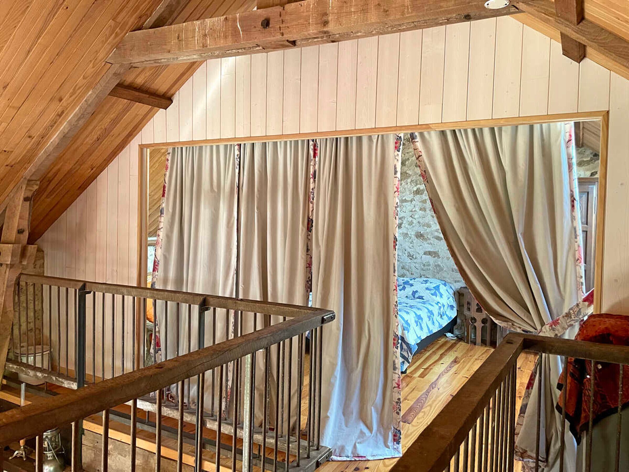 Un escalier en bois avec des rampes en métal menant à une chambre à coucher équipée d’un lit et de rideaux.
