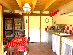 Een keuken met een rode en witte geruitte spatwand, een klok en rode pannen die hangen.
