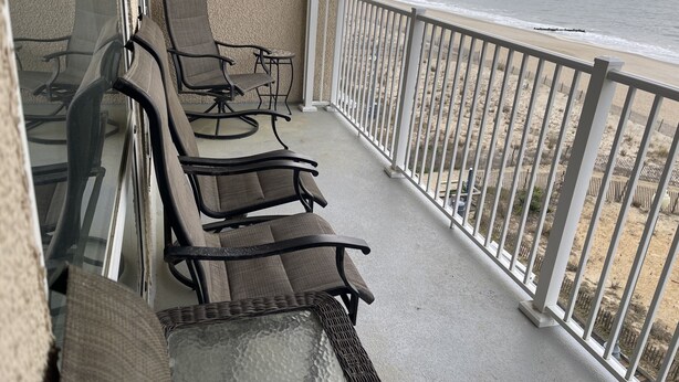 Een balkon met vier stoelen en een tafel, met uitzicht op een strand met een hek en een houten steiger.