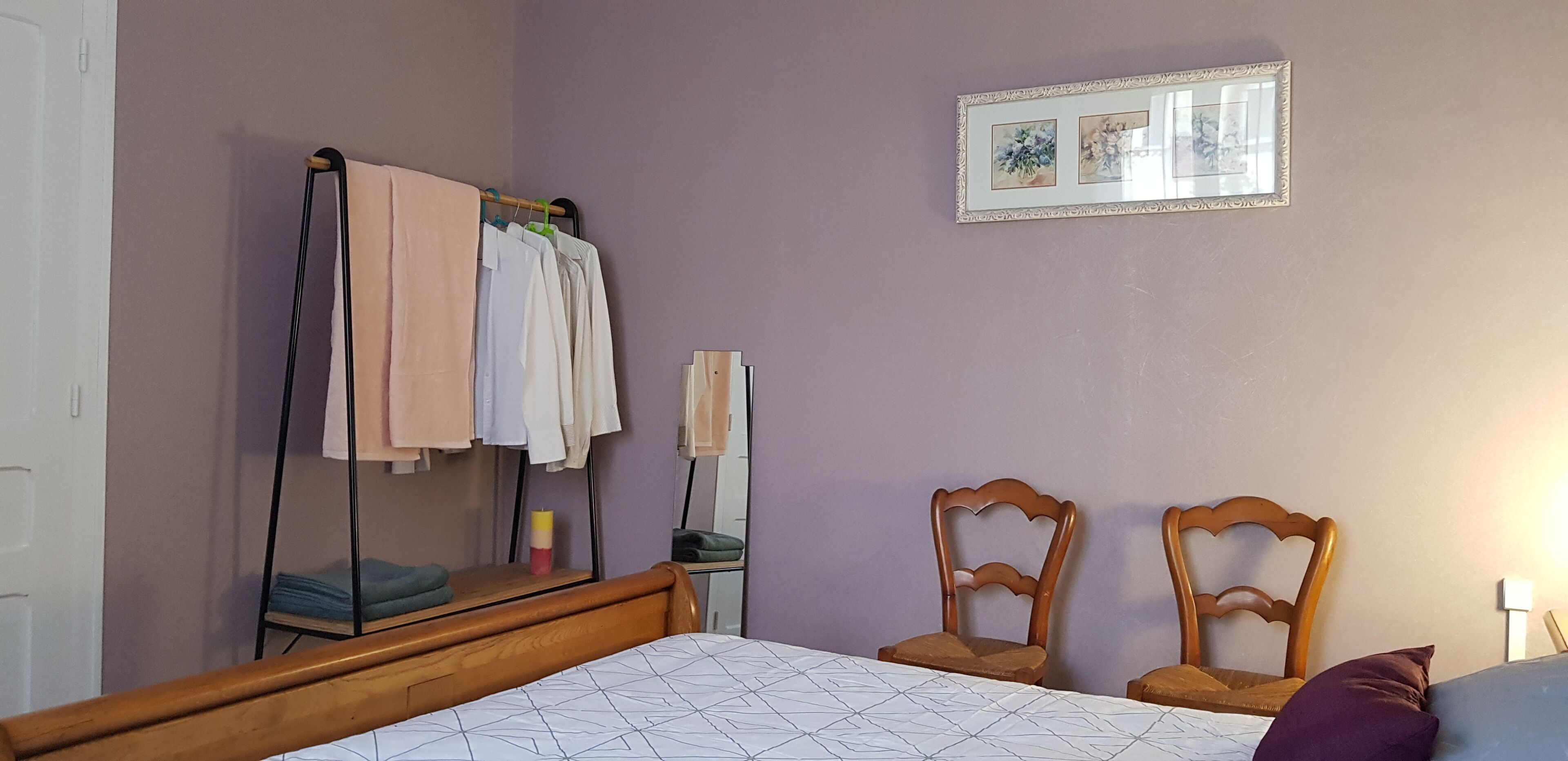 Une chambre à coucher avec un lit, des chaises en bois, une armoire et un miroir au mur.