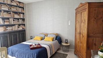 Een slaapkamer met een bed, een boekenkast, een kledingkast en een klein rond tafeltje met een lamp.