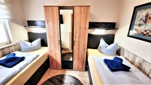 Habitación de hotel con dos camas individuales, un armario de madera, un radiador y una obra de arte enmarcada en la pared.