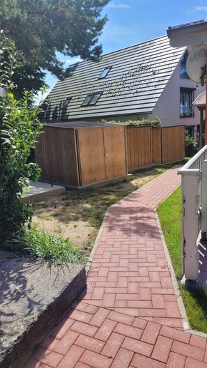A residential area with a paved walkway, wooden fences, and a house with a sloped roof.