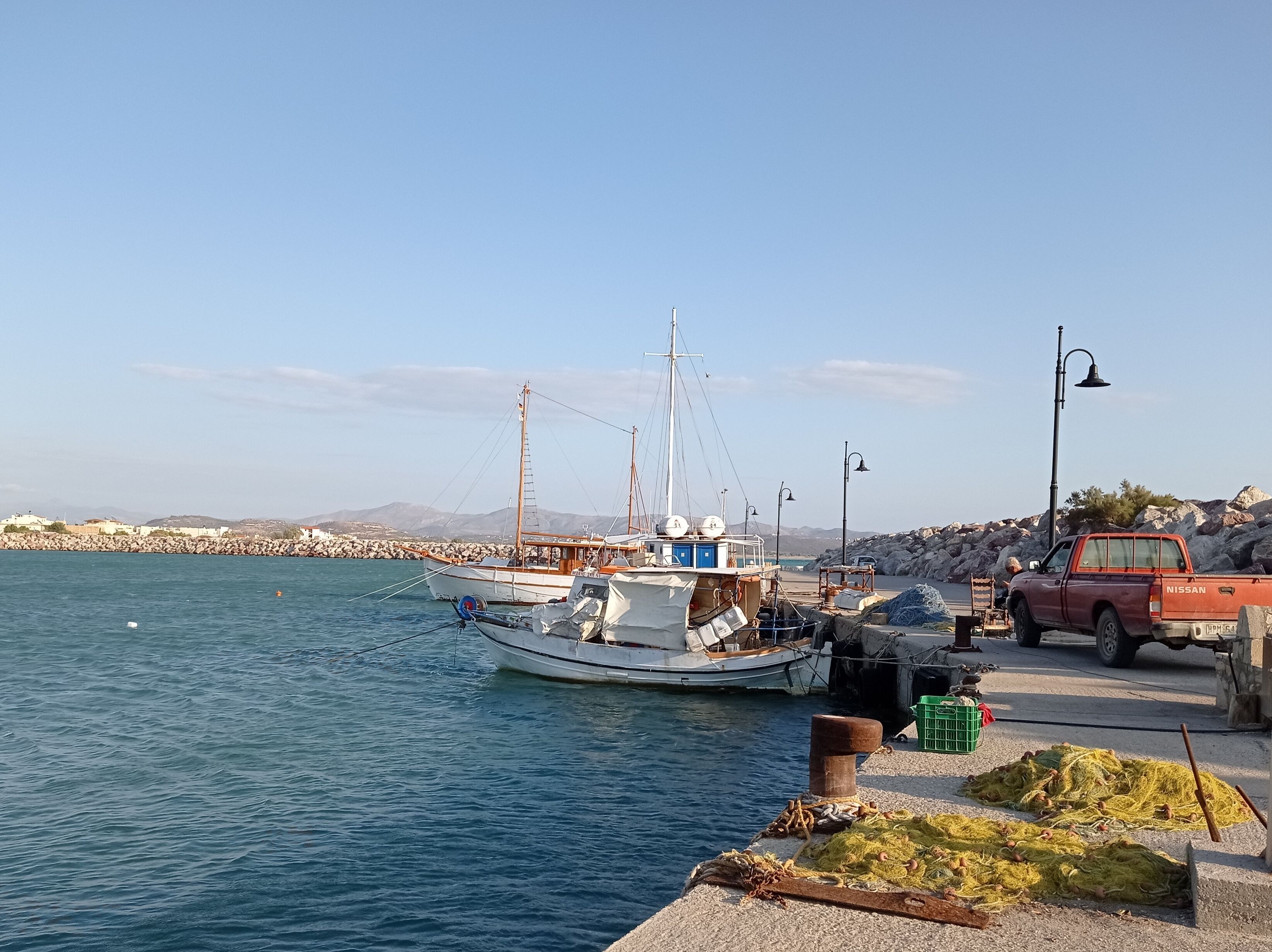 A harbor with a fishing boat docked, a red truck, and fishing nets on the shore.
