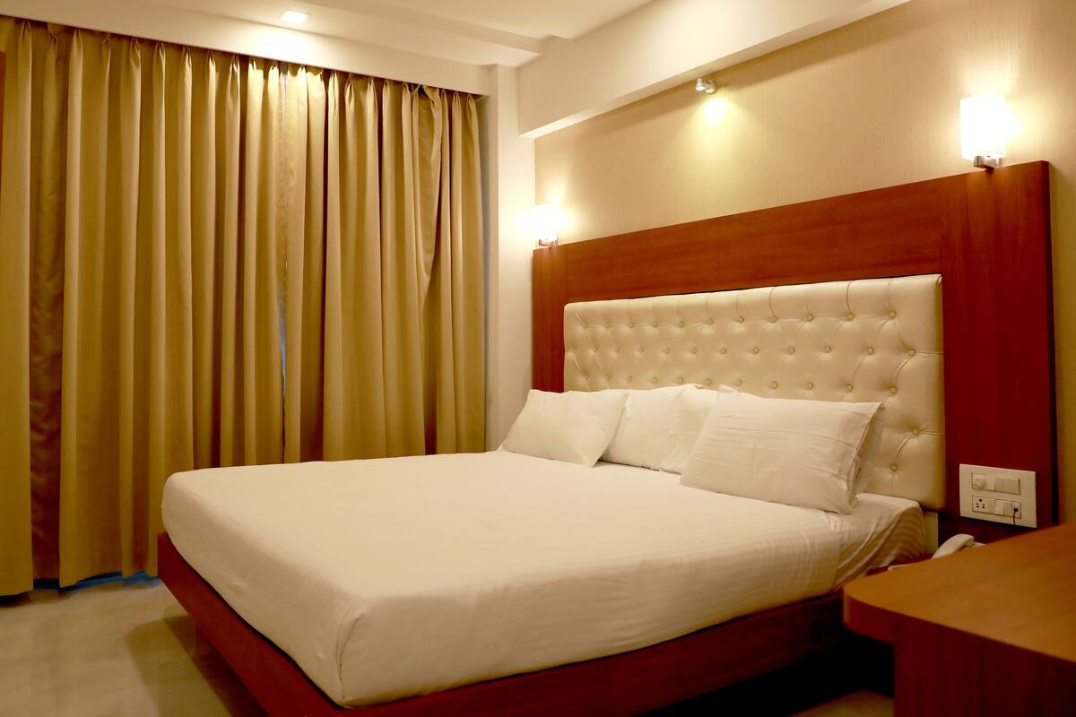 A hotel room with a large bed, a wooden headboard, a bedside table, and a window with curtains.