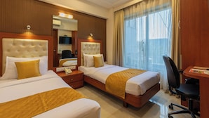 A hotel room with two beds, a desk, a chair, and a large window with curtains. - Hotel Lords Mumbai (Mumbai)