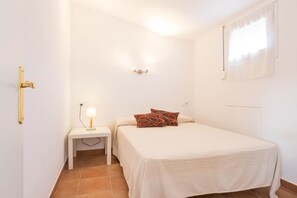 A small, clean bedroom with a single bed, a bedside table with a lamp, and a window with curtains.