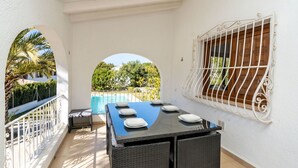 Un balcon avec une table et des chaises, une vue sur une piscine et une rambarde blanche.