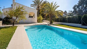 Une piscine à l’eau d’un bleu cristallin, entourée d’une pelouse bien entretenue et de palmiers.