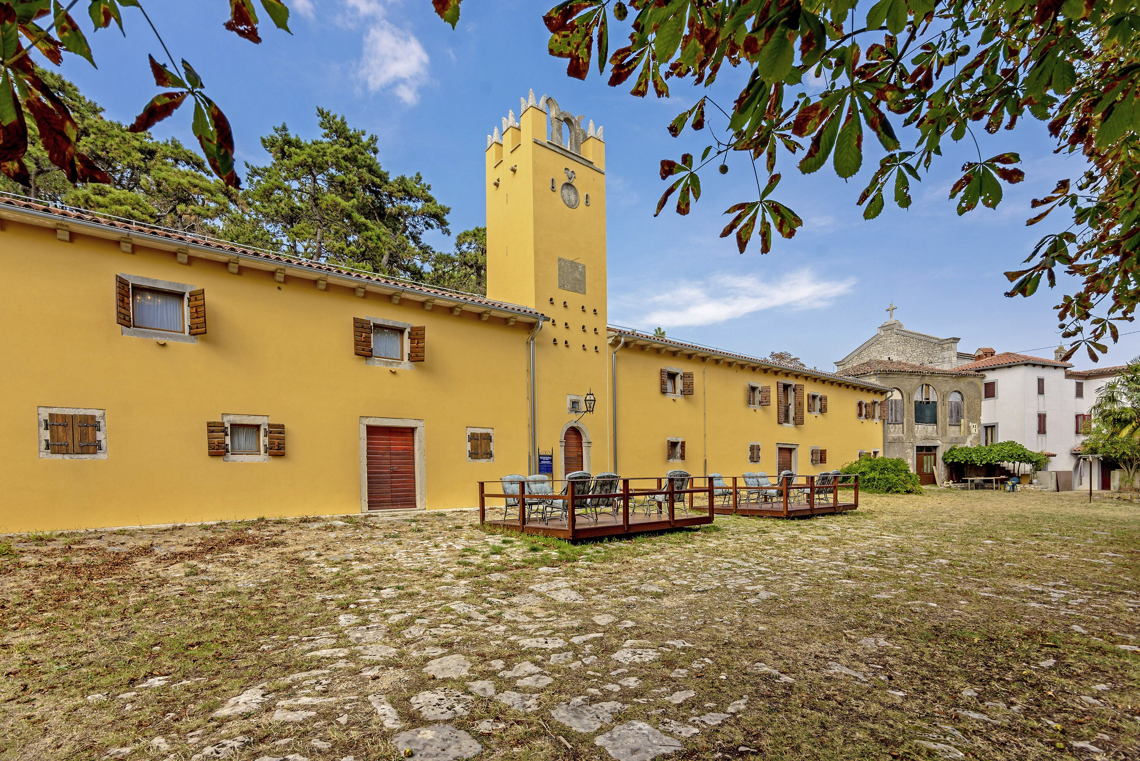 A courtyard with a yellow building, a clock tower, and a stone-paved area.