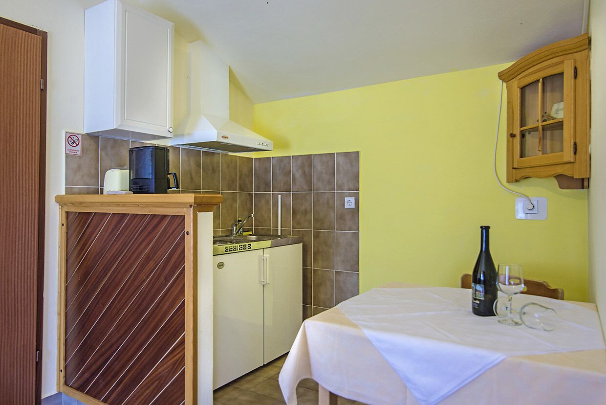A compact kitchen with a sink, cabinets, and a dining table set with a wine bottle and glass.