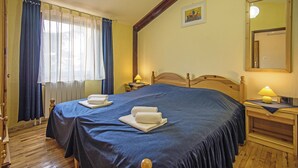 Un dormitorio con una cama grande, dos mesitas de noche con lámparas, un cabecero de madera, una ventana con cortinas y un cuadro en la pared.