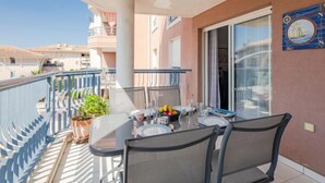 A balcony with a table set for two, potted plants, and a sliding glass door. - Royal Marine by Interhome (Fréjus)