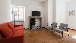Een moderne woonkamer met een open haard, een bank, twee fauteuils en een televisie.