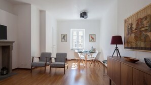 Een ruime woonkamer met een houten vloer, een open haard, een eethoek met een tafel en stoelen, en een groot schilderij aan de muur.