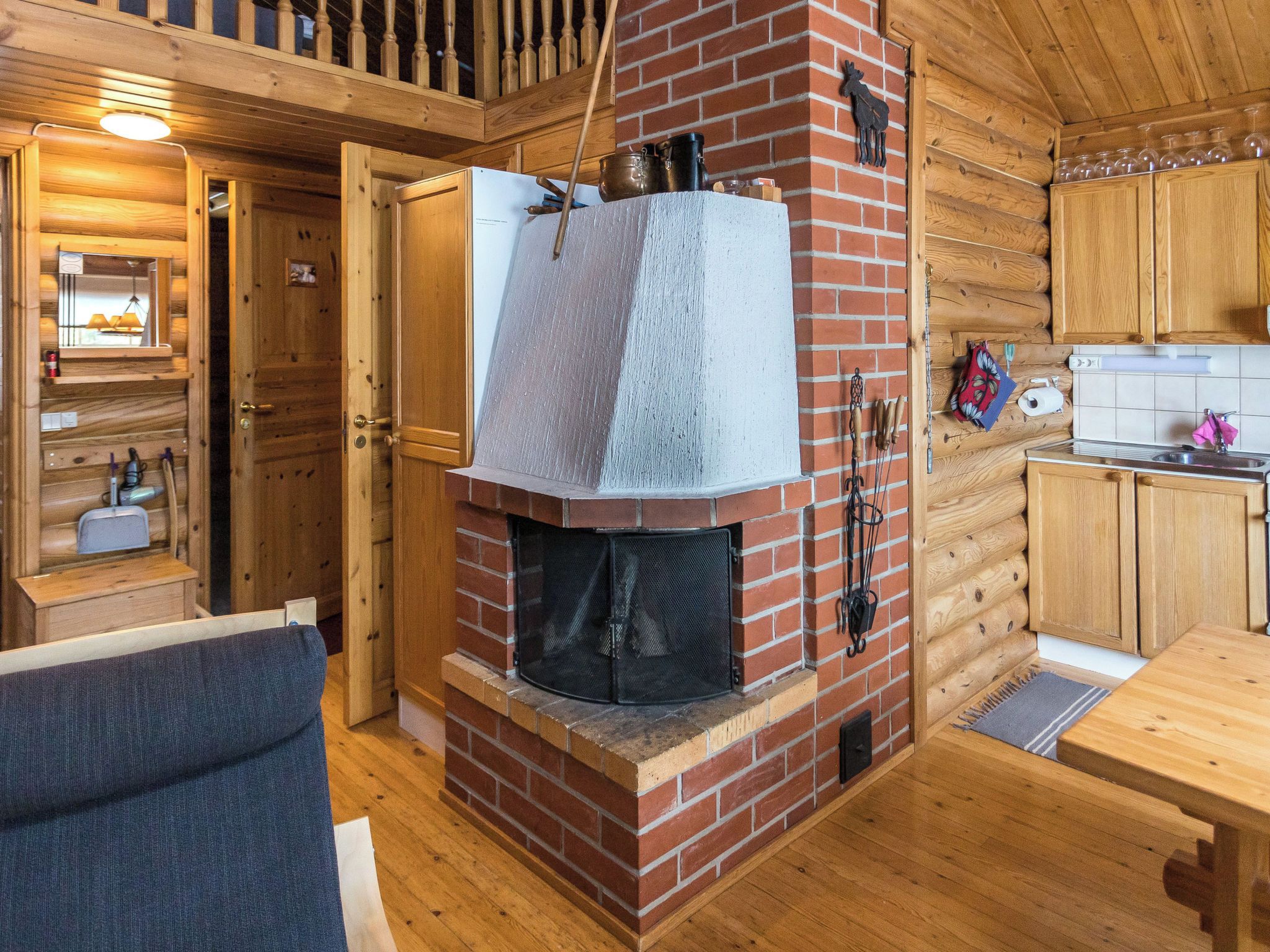A cozy cabin interior with a fireplace, wooden walls, a kitchen area, and a seating space.