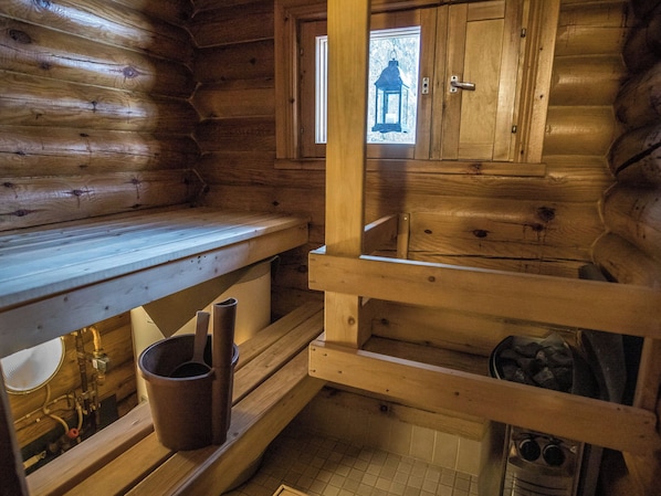 A wooden cabin interior with a bench, a fireplace, and a window with a view of a forest.