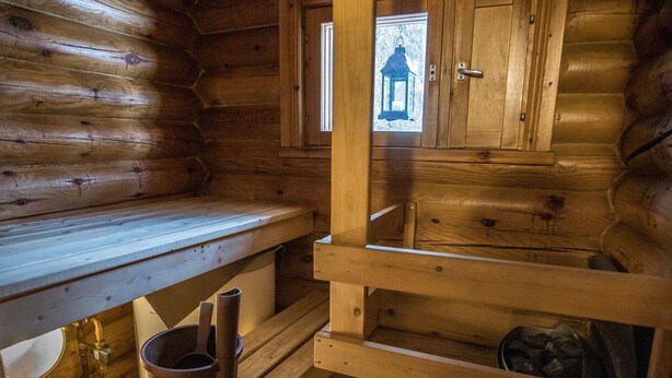 A wooden cabin interior with a bench, a small window with a lantern, and a wooden door. - Jänkäluppo 1 by Interhome (Äkäslompolo)