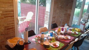 A dining table with various food items and drinks, surrounded by chairs, in a room with large windows. - B&B Au Clair Du Loup (Saint-Loup)