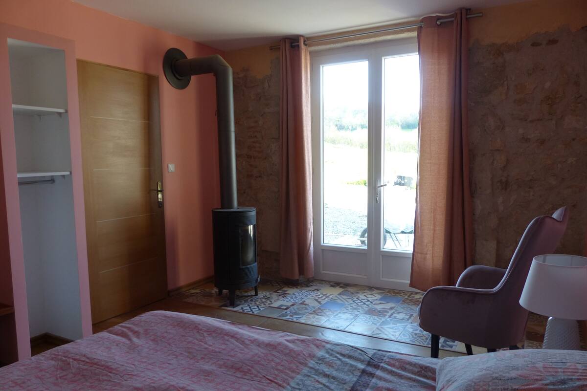 Ein Schlafzimmer mit einem Bett, einem Sessel, einem Kleiderschrank und einem Kaminofen.