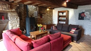 Un salon chaleureux avec un mur en pierre, une cheminée, une bibliothèque et un canapé rouge.