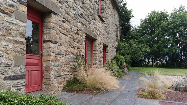 Un bâtiment en pierre avec des portes rouges et un chemin de pierre menant à l’entrée.