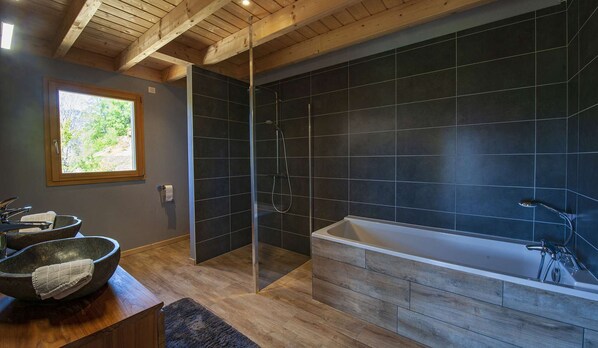Un baño moderno con ducha envuelta en vidrio, una bañera independiente y un tocador de madera con lavabo.