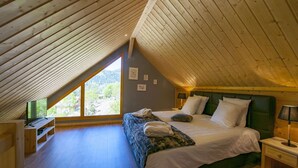 A bedroom with a sloped ceiling, a bed with white bedding, a green headboard, and a window overlooking greenery. - Inuï Grand Chalet - 5-star luxury spa (Muhlbach-sur-Munster)