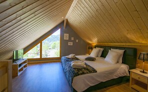 Une chambre avec un plafond en pente, un lit avec une literie blanche, une tête de lit verte et une fenêtre donnant sur la verdure.