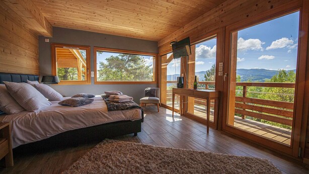 A bedroom with a bed, a chair, a table, and a large window offering a view of the outdoors. - Inuï Grand Chalet - 5-star luxury spa (Muhlbach-sur-Munster)