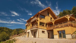 A two-story wooden house with a balcony, large windows, and a sloped roof. - Inuï Grand Chalet - 5-star luxury spa (Muhlbach-sur-Munster)