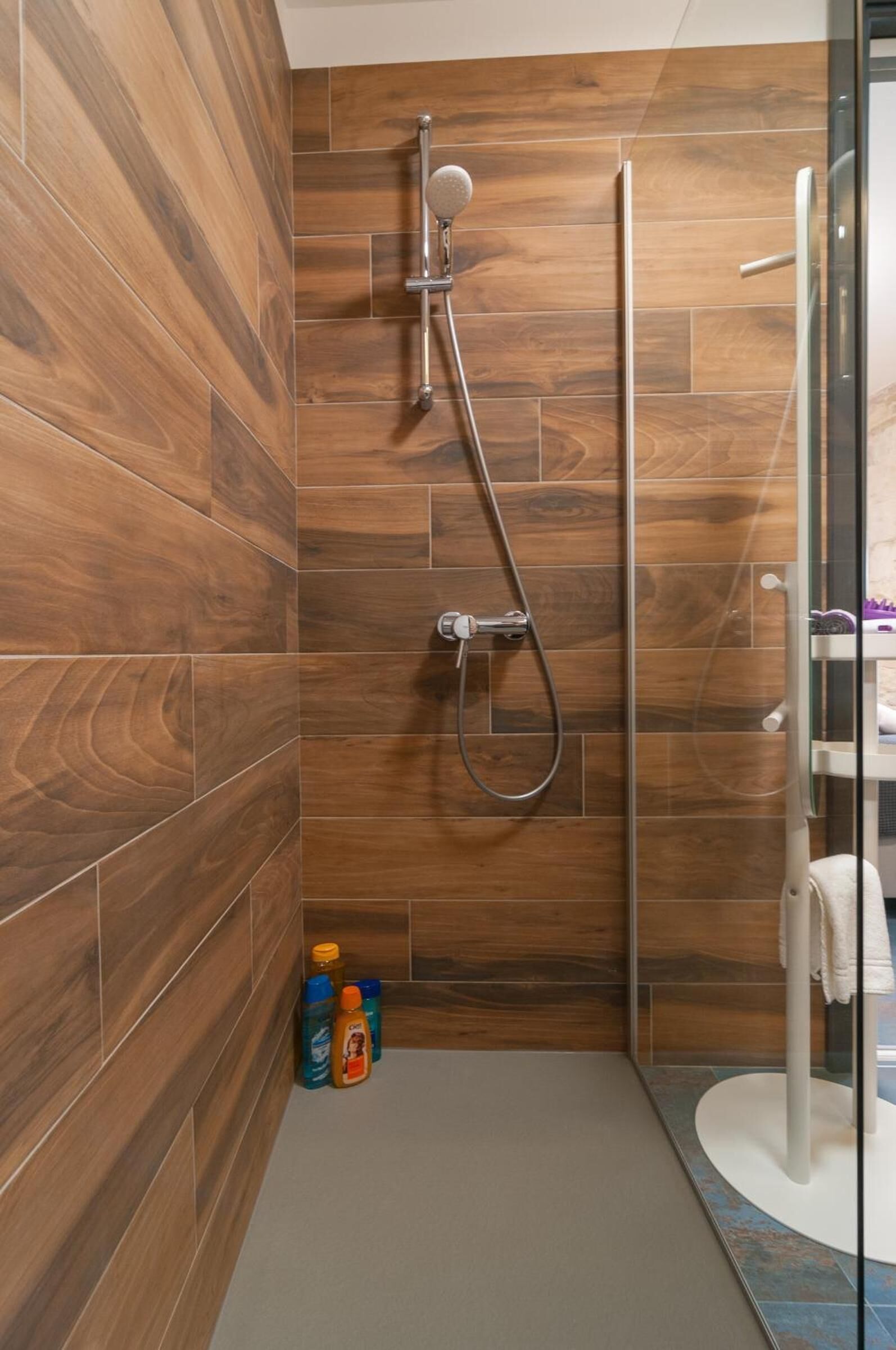 A shower with a wooden wall and a glass door.