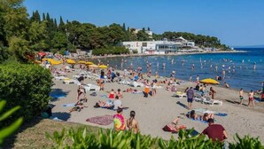 A beach with numerous sunbeds and umbrellas, a clear blue sea, and buildings in the background. - 7heaven Luxury Rooms Palace (Split)