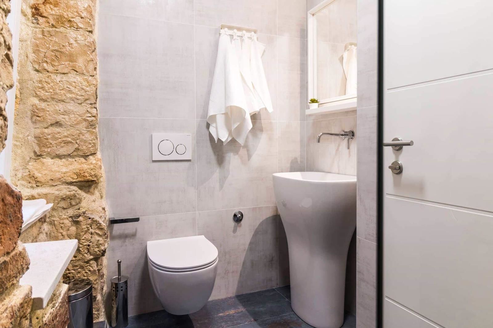 Un baño con inodoro, lavabo y pared de piedra.
