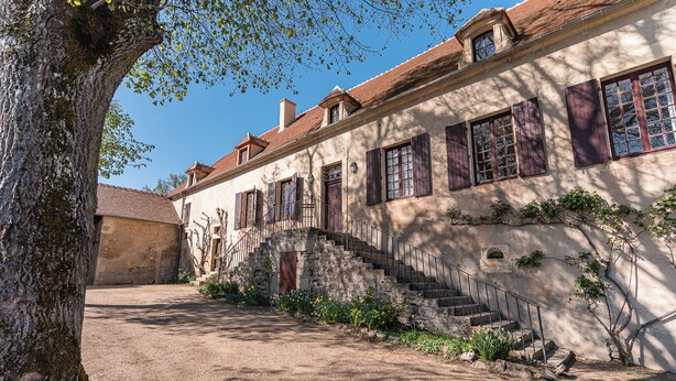 A traditional stone building with a staircase leading to a wooden door, surrounded by a gravel courtyard and a large tree. - Beautiful 1900 Demeure with swimming pool and enclosed garden, in a charming village (Apremont-sur-Allier)