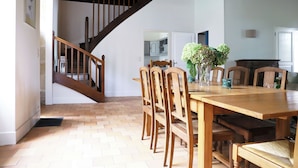 A dining area with a wooden table and chairs, a staircase, and a view into the kitchen. - Beautiful 1900 Demeure with swimming pool and enclosed garden, in a charming village (Apremont-sur-Allier)