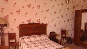 Een slaapkamer met een houten bed, een houten stoel, een houten kledingkast en een spiegel aan de muur.