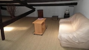 Een kamer met een houten bankje, een witte leren bank, een kleine tafel en een radiator.