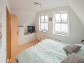 A bedroom with a bed, a TV, a wardrobe, and two windows. - Vacation home Jähnert, vacation rental North Sea - Holiday home Jähnert (Varel)