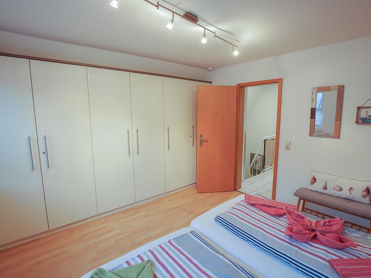 Een slaapkamer met een grote inbouwkast, een bed met gestreepte beddengoed, en een houten deur.
